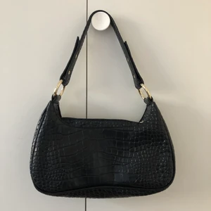 Handväska - Väska i krokodilimitaton från Nelly. Justerbart axelband. Endast använd en gång.