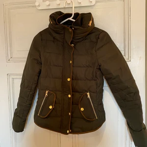 Tajt dunjacka i storlek 24/xs  - Mörkgrön dunjacka med gulddetaljer. Passformen är figurnära, storlek 34/xs 