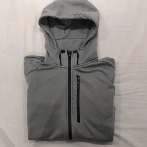 Adidas Hoodie Strl. S - Grå hoodie från Adidas i manlig passform. Passar bra som träningströja men även till vardags. Inga fläckar, inga skador bortsett från det lilla hål som syns i första bilden. Två innerfickor finns också. Säljer på grund av att jag inte använder den längre. 