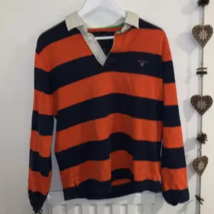 Orange och mörkblå Gant tröja, perfekt om du vill ha en preppy stil med lite färg! Vit krage med tre knappar så man bestämmer hur djup urringning det är