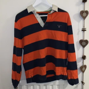 Gant tröja - Orange och mörkblå Gant tröja, perfekt om du vill ha en preppy stil med lite färg! Vit krage med tre knappar så man bestämmer hur djup urringning det är