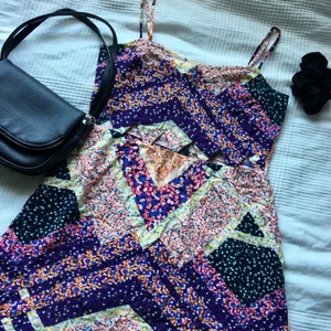 Blommig sommar/ strandklänning - Supersöt sommar/ strandklänning i ett lätt flowigt material och blommor i olika färger. Kort i modellen med triangelformade hål framtill i midjan. Den har används endast ett par gånger och är i nyskick. Storleken är 40.