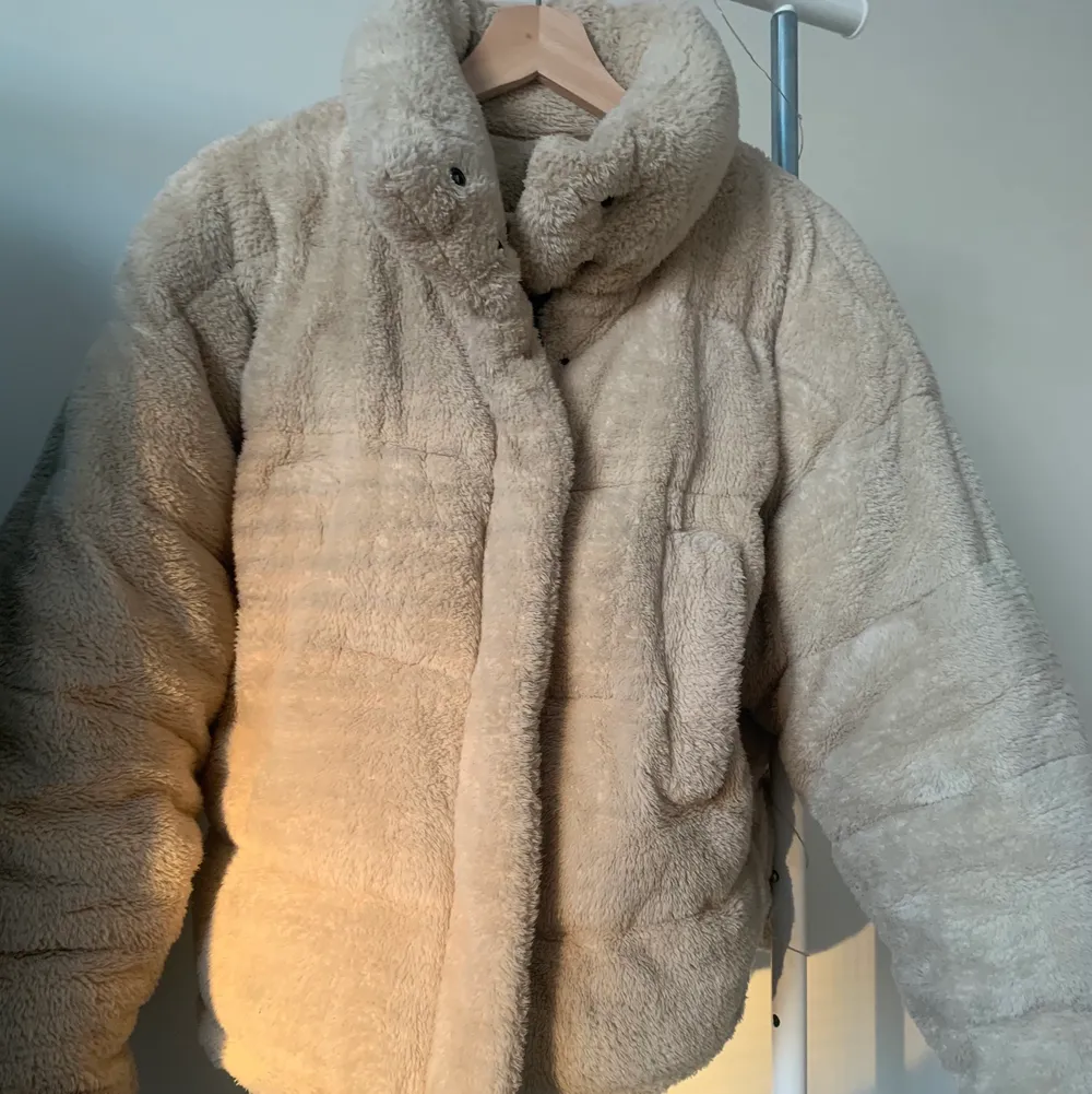 Urban outfitters beige puffer jacket. The outside is fluffy with synthetic fur-like material, very soft and cozy. The inside is lined with polyester and cotton blend. The puffer jacket is warm and a perfect spring transition piece. Fits just below the waist. There is a zipper and buttons that go up to the neck. The collar can be buttoned up to cover the neck. Has two side pockets, one of which has a hole in the lining that can be easily fixed. Size is XS, but can also fit S as it is oversized.. Jackor.