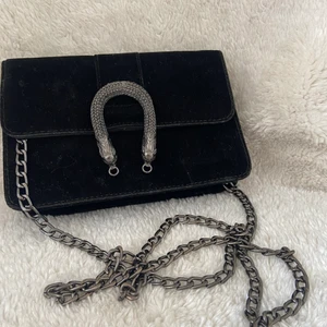 Fin väska - Fin väska i svart tyg med prydnad fram samt metallkedja. Stängs med magnet framtill. Ett stort fack.
