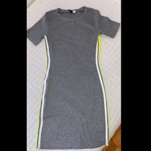 Grå klänning  - Säljer denna simpla & fina sommar med 2 vit och neon gula ränder på vars sida av klänningen. Jag köpte den från H&M för 149kr och säljs för 50 kronor. Den är i storlek S men passar perfekt för storlek M. Kan mötas i Trelleborg vid köp annars står köparen för frakten! 