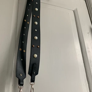Svart väsk rem - Svart Väsk rem med vita och brons färgade detaljer, passar till allt. Kan skicka men köparen står för frakt:)