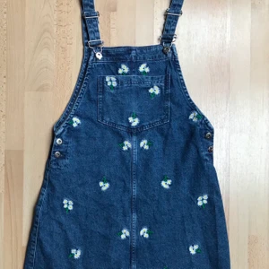 Hängselklänning med broderade tusenskönor  - Väldigt söt hängselklänning från H&M. Nästan 3 år gammal men använd max 2 gånger. Kameran på min telefon suger men kan skicka närbild på broderiet om önskas. 