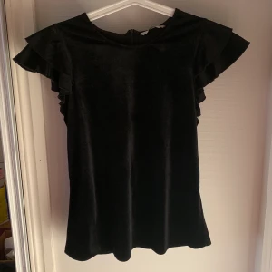 T-shirt  - Svartglittrig T-shirt med volangärmar. Storlek 36