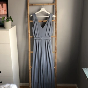 Ljusblå byxdress Bik Bok storlek M - Byxdress i skönt material. Från Bik Bok. v-ringad i bak med dragkedja. Blå till färgen i den lite gråare tonen som syns på bild mot den grå väggen. Superfin och skön!