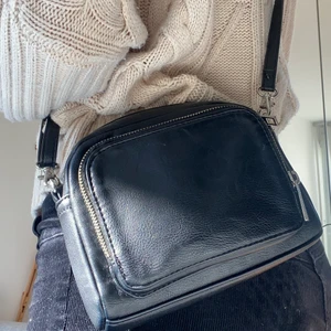 Svart handväska  - Jag säljer min svarta handväska i fakeskinn som är väldigt smidig att ha med sig. Den har avtagbara och justerbara band och två fack med dragkedjor. Frakten ingår i priset:) 