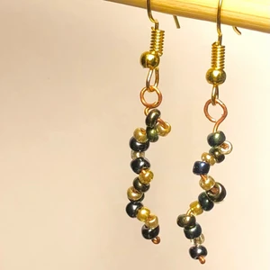 Örhängen, handgjorda, en helix av pärlor - Handgjorda örhängen i form av en helix/ spiral av koppartråd med glaspärlor. Örkrokar av gulmetall. 