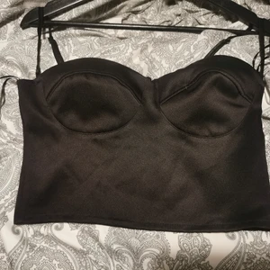 Bustier topp  - Svart croppad bustier topp från Gina Tricot i satin ish material. Avtagbara axelband och silikon längst uppe på kupan vilket gör att den håller sig på plats. Även resår i ryggen vilket ger en bra passform! 