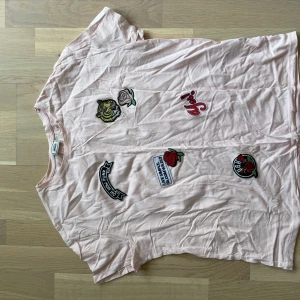 T-shirt med påsydda märken - En ljusrosa T-shirt storlek M. Nyskick.