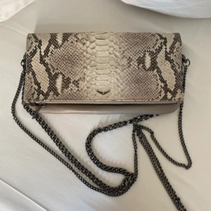 Zadig & Voltaire väska! - Zadigväska i ormskinnsimitation! Måtten är 27x13x2. Jag har inte använd väskan särskilt mycket så skulle säga att skicket ändå är bra. Bilderna är rättvisande så kolla på dom!! Inuti det största facket finns en blå liten fläck från en penna men det är ingenting som syns alls!