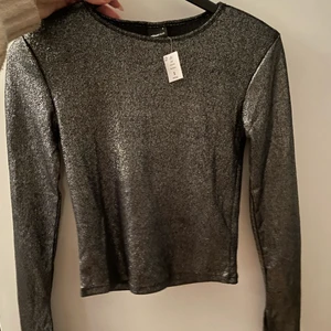 Glittrig festtopp - Oanvänd glittrig topp från Gina tricot, toppen har axelvaddar och slits i armarna. Storlek s