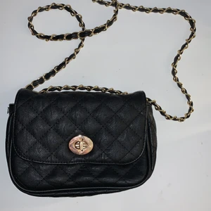 Svart handväska - Svart väska i fakeläder med gulddetaljer. Långt band men går att vika kortare. Flera fack inuti, lite använd