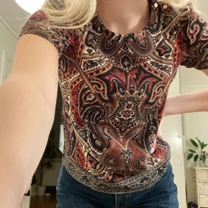 Superfin mönstrad tshirt - Supercool tshirt som är mönstrad från Oasis (färgen gör sig mest rättvisa på bild 2), har knappar på ena axeln och ett svart ”band” i mitten av ryggen (bild 2). Storlek 34, köparen står för frakten