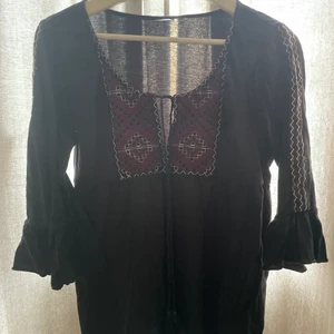 Blus - En svart blus med lila och vita detaljer. Ränder längst armarna. Den har knyte på bröstet för att få mer eller mindre urringning. S/M. Passar mig som kan ha både S och M