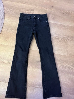 Svarta bootcut jeans från Kappahl - Snygga svarta jeans från Kappahl i storlek 158. Modellen har klassisk femficksdesign, normal midja och bootcut-ben som ger en schysst siluett. Materialet är mjukt och stretchigt för extra komfort. Perfekta till sneakers eller boots.