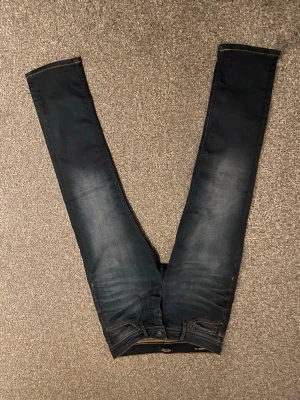 Jack & Jones Slim Straight Tim jeans - Mörkblå jeans från Jack & Jones i modellen Slim Straight Tim. Klassisk femficksdesign med orange kontrastsömmar och knappgylf. Jeansen har en rak men smal passform och är tillverkade i slitstarkt denimtyg.