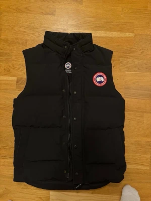Svart dunväst från Canada Goose - Säljer en svart dunväst från Canada Goose med klassisk logga på bröstet. Storlek S men passar M