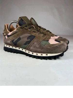 Valentino Rockrunner sneakers camo - Säljer ett par Valentino Rockrunner sneakers med camouflage-mönster i grönt, brunt och beige. Skorna har ovandel i mocka och textil, snörning och coola nitar runt sulan. Grov svart yttersula för extra grepp och edgy look.