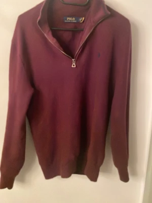 Vinröd half zip tröja Polo Ralph Lauren - Säljer en vinröd långärmad tröja från Polo Ralph Lauren med half zip-dragkedja och liten broderad logga på bröstet. Tröjan är i mjuk bomull och har en klassisk, stilren look som passar perfekt till höst och vinter.