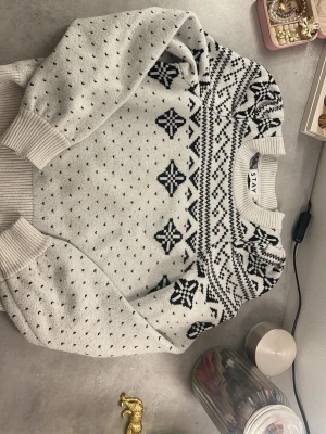 Vit och svart stickad tröja från STAY - Säljer en mysig vit stickad tröja från STAY i storlek XS. Tröjan har svart mönster med nordisk vibe, ribbade muddar och rund hals. Perfekt för kalla dagar och riktigt snygg till jeans eller kjol.🤍🖤