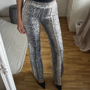 Vida byxor med ormmönster - Snygga vida byxor med grått och svart ormmönster. Byxorna har hög midja och raka ben.