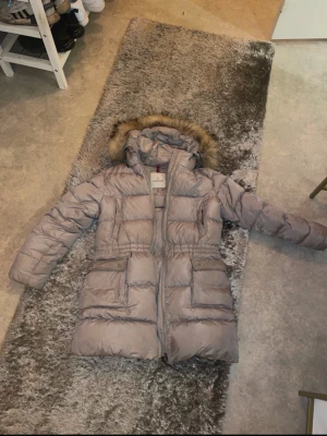 Beige Moncler dunjacka med pälskant - Säljer en beige dunjacka från Moncler med huva och pälskant. Jackan har flera stora fickor framtill. Perfekt för kalla dagar och riktigt snygg till vintern. Klassisk Moncler-detalj på insidan. Nytt pris:9000