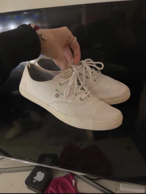 Vita sneakers från Gant - Säljer ett par klassiska vita sneakers från Gant med snörning. Skorna har en stilren design med rund tå, diskret logga på sidan och ovandel i bomullstyg. Yttersulan är vit med mörkblå undersida skulle jag säga. 