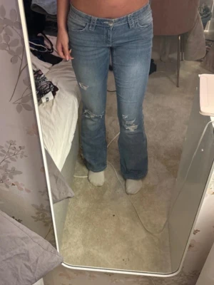 Blå bootcut jeans med broderad ficka - Säljer ett par ljusblå bootcut jeans med slitningar på låren och knäna. Jeansen har låg midja och snyggt broderi på bakfickan. De är från Gina Young i storlek 164, de passar mig som är 168 💕säljer för har inte kommit till användning 