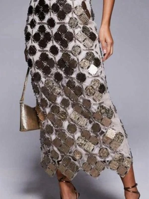 Glittrig långklänning med paljetter - Un contemplativ insyn i en långklänning med stora fyrkantiga paljetter i silver och guld på ett ljust tyg. Klänningen upprättar en unik look med öppen rygg, snörning och slits bak. Perfekt för dig som vill sticka ut.