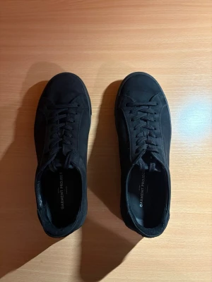 Garment Project Sneakers (nubuck-läder) - Ett par svarta skor från Garment Project i nubuck-läder, storlek 40.  Skorna är väldigt varsamt använda och i princip nyskick. Enda anmärkningen är ett litet snitt vid hälen (vänster sko), syns knappt i verkligheten (se bild).  Butikspris 1800kr.  Material: • Överdel: 100% nubuck • Foder/övre foder: 100 % läder • Innersula: polyuretan-skum • Yttersula: gummi 