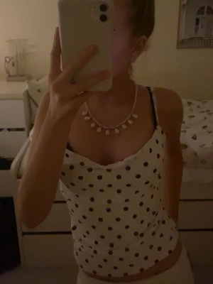 Vit prickig linnetopp från Amisu - Supersöt vit linnetopp med svarta prickar från Amisu. Toppen har tunna axelband och en snygg draperad urringning. Perfekt för varma dagar och enkel att styla med jeans eller kjol.