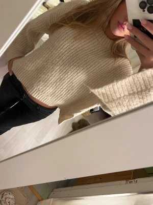 Beige stickad tröja med vida ärmar - Säljer en beige stickad tröja med bred ribbad struktur och vida, långa ärmar. Tröjan har en sopren, croppad passform och hög halsringning. Perfekt för dig som gillar en avslappnad men ändå trendig look.