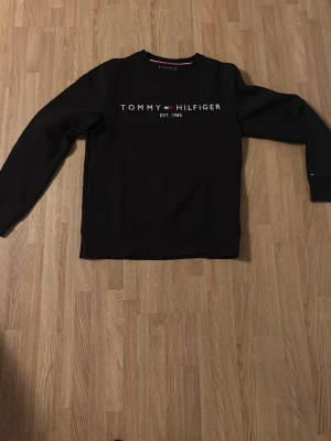 Svart sweatshirt Tommy Hilfiger - Säljer en svart sweatshirt från Tommy Hilfiger med logga och text framtill. Tröjan har långa ärmar och klassisk rund hals. Detaljer med röd och vit rand på insidan av kragen. Perfekt för en clean och stilren look. Har inte använt den ofta. Pris kan diskuteras.