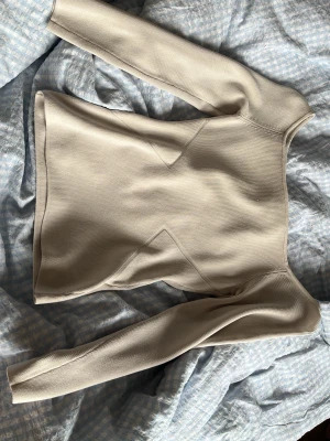 Beige ribbad topp från H&M - Säljer en beige ribbad topp från H&M i storlek S. Toppen har lång ärm, fyrkantig urringning och markerade sömmar framtill som ger en snygg detalj. Materialet är stretchigt och följsamt, perfekt till jeans eller kjol.