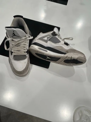 Nike Air Jordan 4 Retro Vit/Svart - Säljer ett par Nike Air Jordan 4 Retro i vitt och svart med meshpaneler och klassisk Jumpman-logga på plösen och hälen. Skorna har snörning, platt sula och detaljer i mocka och skinn. Perfekta för dig som vill ha en ikonisk sneaker med streetwear-vibe. Om du vill pruta skriv till mig 