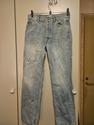 Ljusblå raka jeans med slitning - Säljer ett par ljusblå jeans från Perfect Jeans (Gina Tricot) med klassisk femficksdesign och raka ben. Jeansen har en tydlig slitning på vänster lår för en extra vintagekänsla. Hög midja och robust denim i bomull gör dem perfekta för en avslappnad look.
