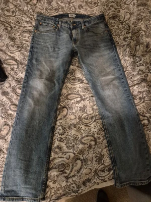 Lager 157 blå jeans W36 L32 - Klassiska lager 157 jeans i ljusblå tvätt med raka ben och fem fickor. Jeansen har orange sömmar och är tillverkade i slitstarkt denim. Perfekta för dig som gillar en tidlös look och vill ha ett par jeans med bekväm passform.