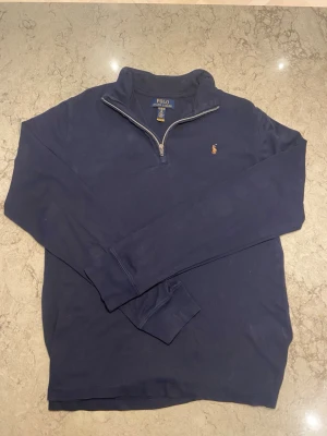 Marinblå half zip tröja Polo Ralph Lauren - Säljer en marinblå långärmad tröja från Polo Ralph Lauren i storlek XL. Klassisk half zip med dragkedja och ikoniska broderade polospelaren på bröstet. Skön passform och mjukt bomullsmaterial, perfekt till lager på lager under höst och vinter.