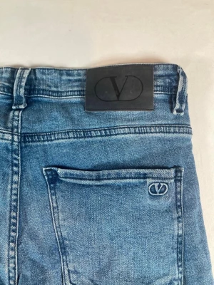 Blå jeans från Valentino, straight fit - Säljer ett par klassiska blå jeans från Valentino med raka ben och normal passform. Jeansen har snygga detaljer som broderad logga på fickan och patch bak i midjan. Tillverkade i mjukt denimtyg med fem fickor och bälteshällor. Storlek är W33 och längden är 102cm. 