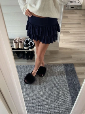 Mörkblå volangkjol med resårmidja - Supersöt mörkblå kortkjol med dubbla volanger och bred resår i midjan. Kjolen har en flowy känsla och är perfekt för dig som gillar en feminin och trendig look. Materialet känns mjukt och följsamt mot kroppen.