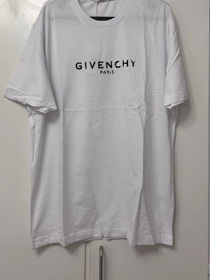 Vit  t-shirt i bomull XXL - Snygg vit t-shirt  svart logotyptryck på bröstet. Klassisk rund halsringning och korta ärmar. Tillverkad i mjuk bomull som känns skön mot huden. Perfekt för dig som gillar stilrena designer och exklusiva märken.