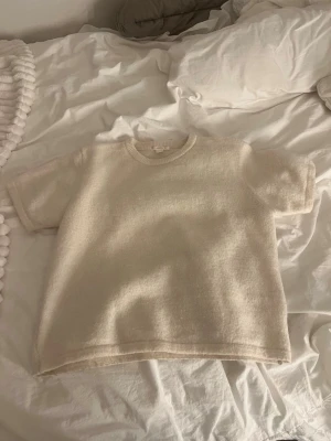 Beige stickad t-shirt från Gina Tricot - Kortärmad stickad t-shirt i beige från Gina Tricot. Tröjan har rund halsringning och en mjuk, lite fluffig struktur. Perfekt för dig som gillar en enkel men ändå cozy look. Passar till både jeans och kjol.