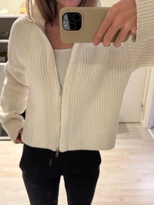 Vit helzip kofta från Bik Bok - Säljer en vit zip kofta från Bik Bok med krage och dragkedja framtill. Koftan är stickad i ett mjukt material och har långärmad passform. Perfekt till lager på lager och enkel att styla till olika outfits.