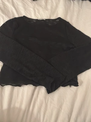 långärmad topp - Säljer en svart mesh topp från Cubus i storlek 158/164. Toppen är långärmad och har en transparent, tunn stickad look med vågig kant nertill. Perfekt för att styla lager på lager eller till ett par snygga jeans.