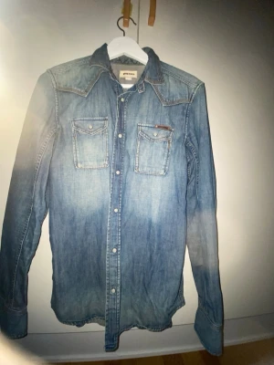 Blå jeansskjorta från Diesel - Säljer en snygg blå diesel jeans skjorta. Väldigt cool och fräsch inför påsken och har en väldigt cool design 