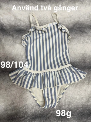 Randig baddräkt med volang - Säljer en söt baddräkt med blå och vita ränder och volangdetalj i midjan. Axelbanden är smala och det finns små volanger vid axlarna. Perfekt för strand eller poolhäng!🌸 Använd två gånger. Storlek 98/104